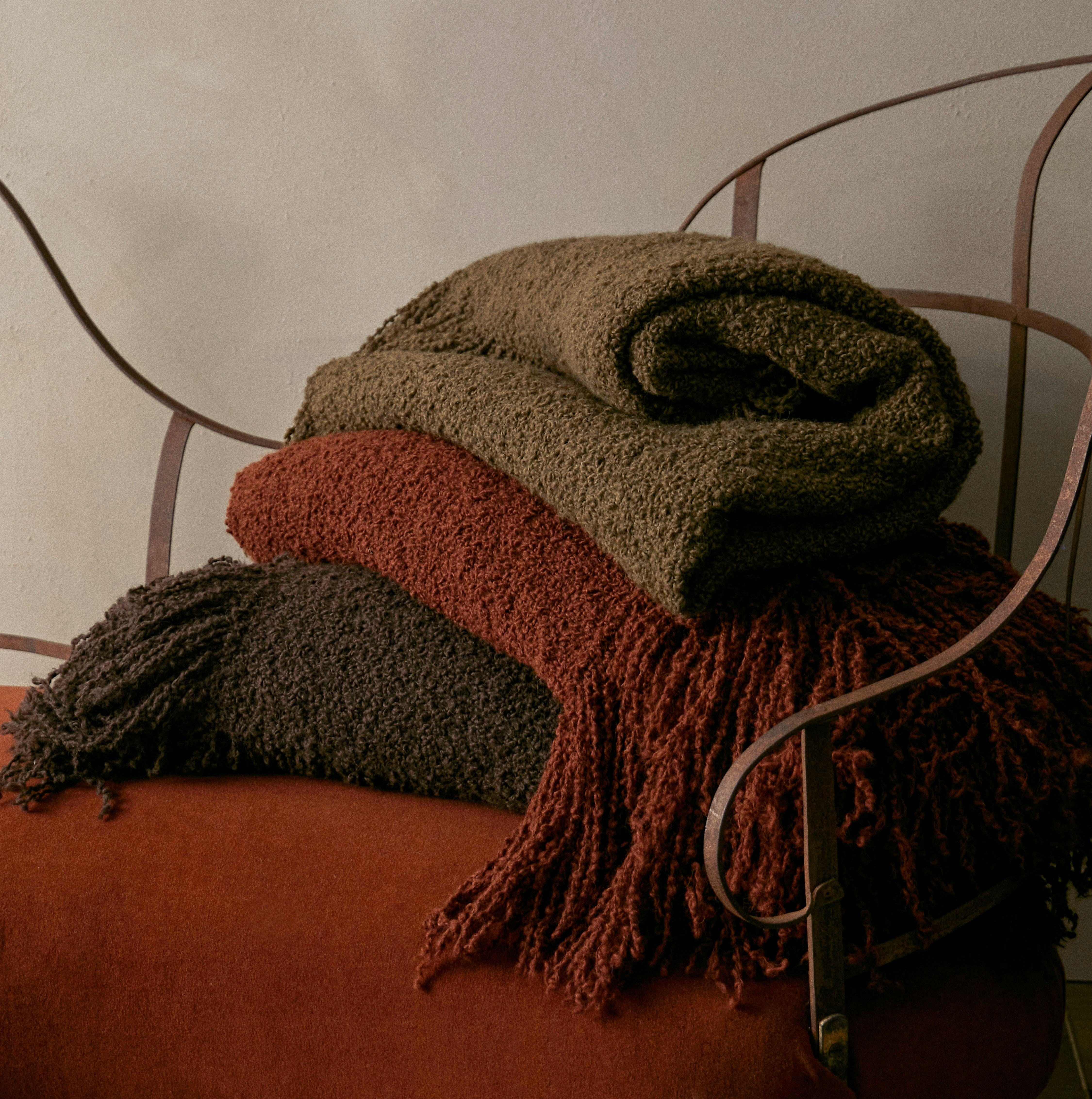 Stack of textured blankets in brown and red on a metal chair against a neutral wall.