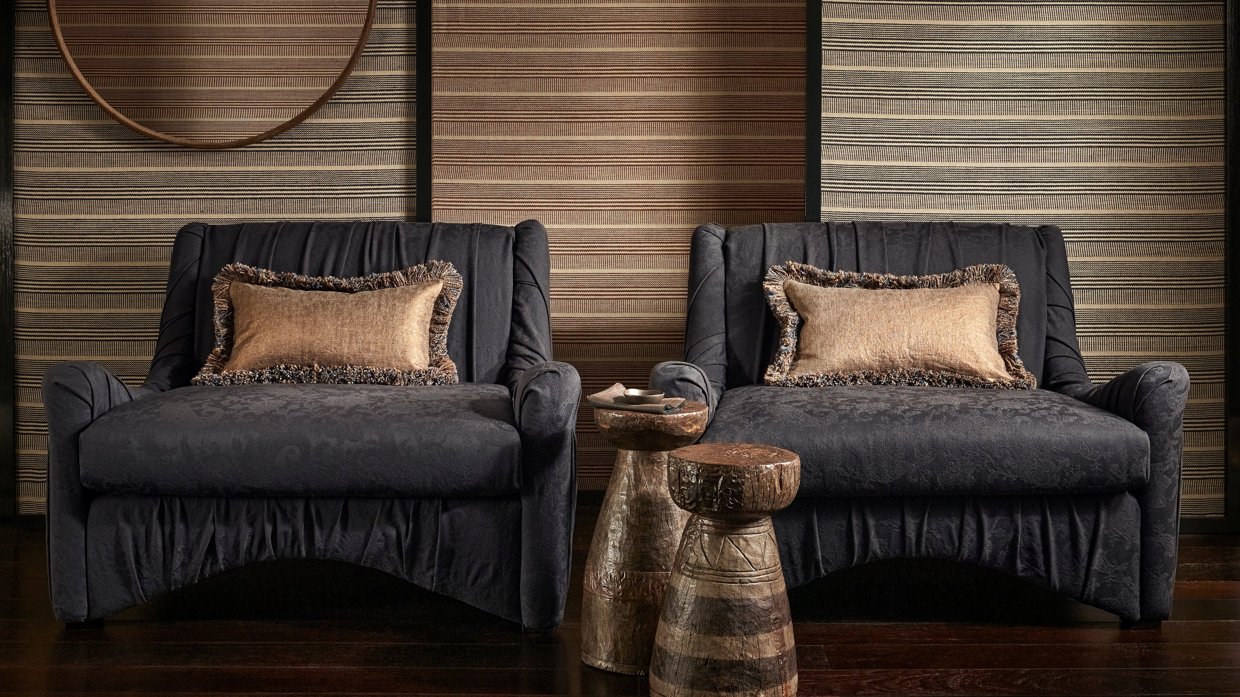 Two navy armchairs with patterned cushions in a room with wooden walls and a round mirror.