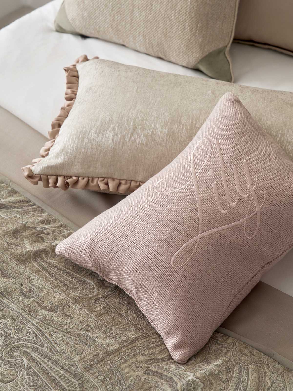 Pink pillow with 'Lilly' embroidery on a sofa with beige cushions.